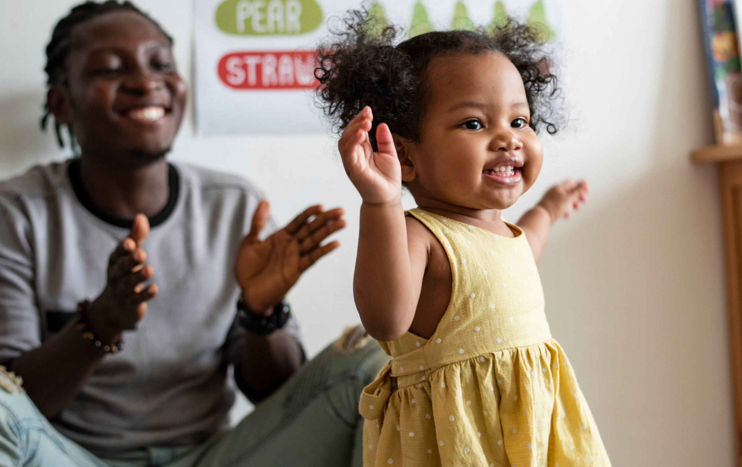 African American woman sitting with hands open while small child tries to walk