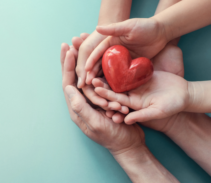 Adult and children hands hold a ceramic red heart.