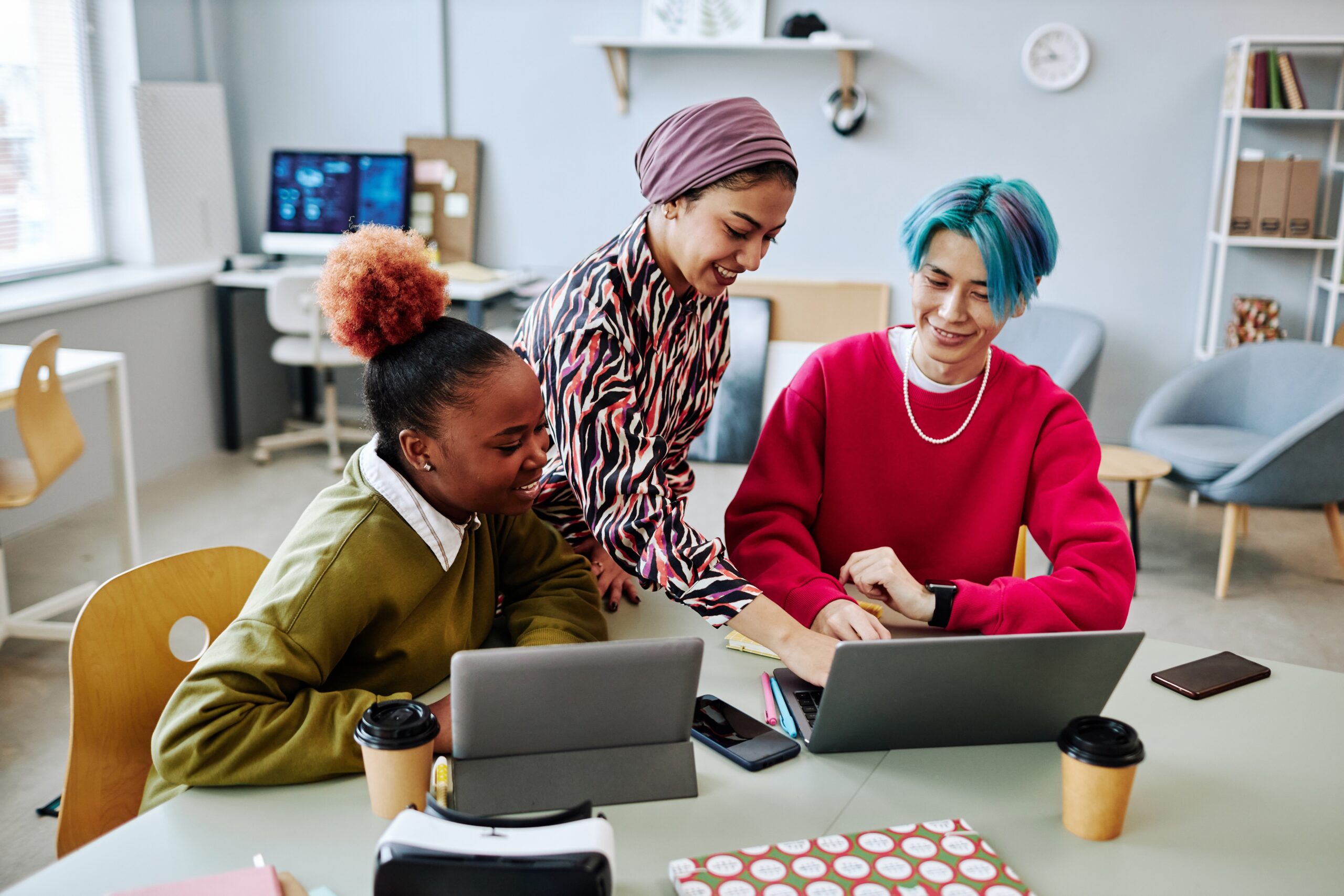 A diverse group of young adults working together at a table with two laptops.