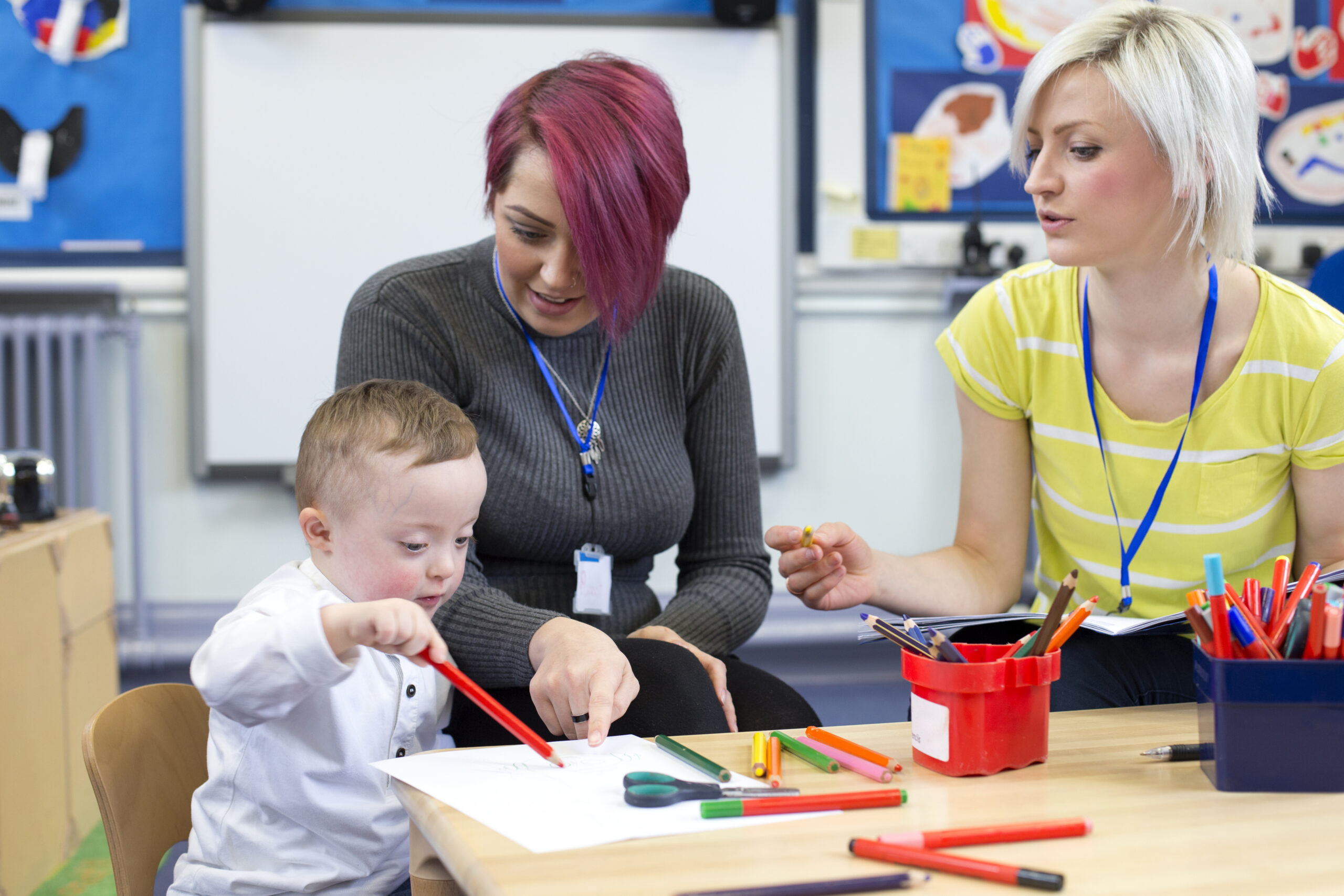Nursery teacher sitting with a parent and her Down Syndrome son in the classroom. they are discussing the little boys progress.