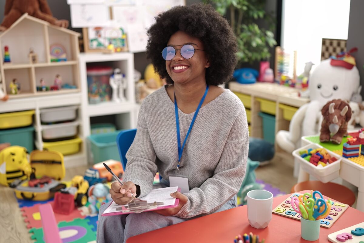 Educator poses for photo in a classroom while completing a form on her clipboard