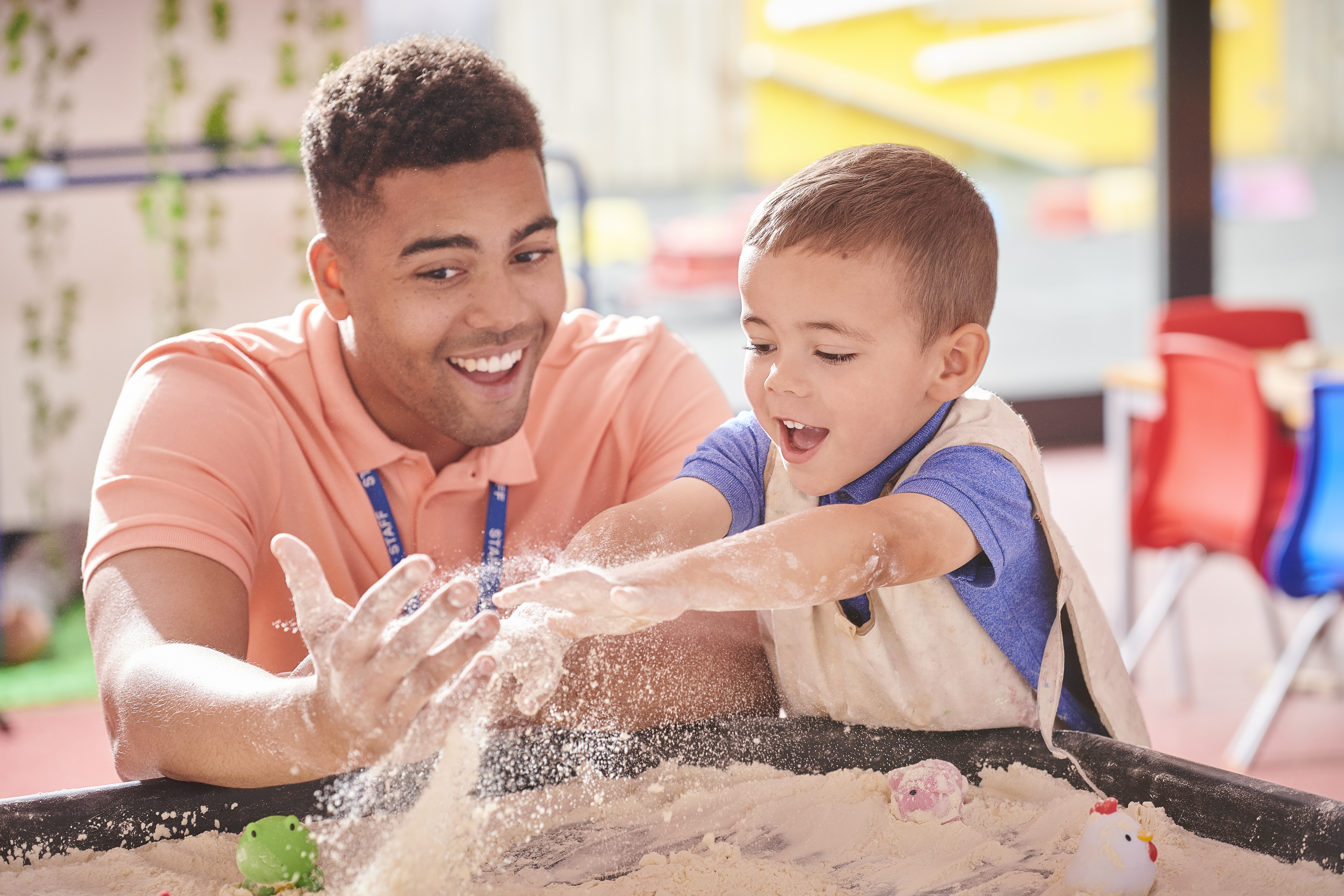 nursery teacher and young student playing in an indoor sandpit