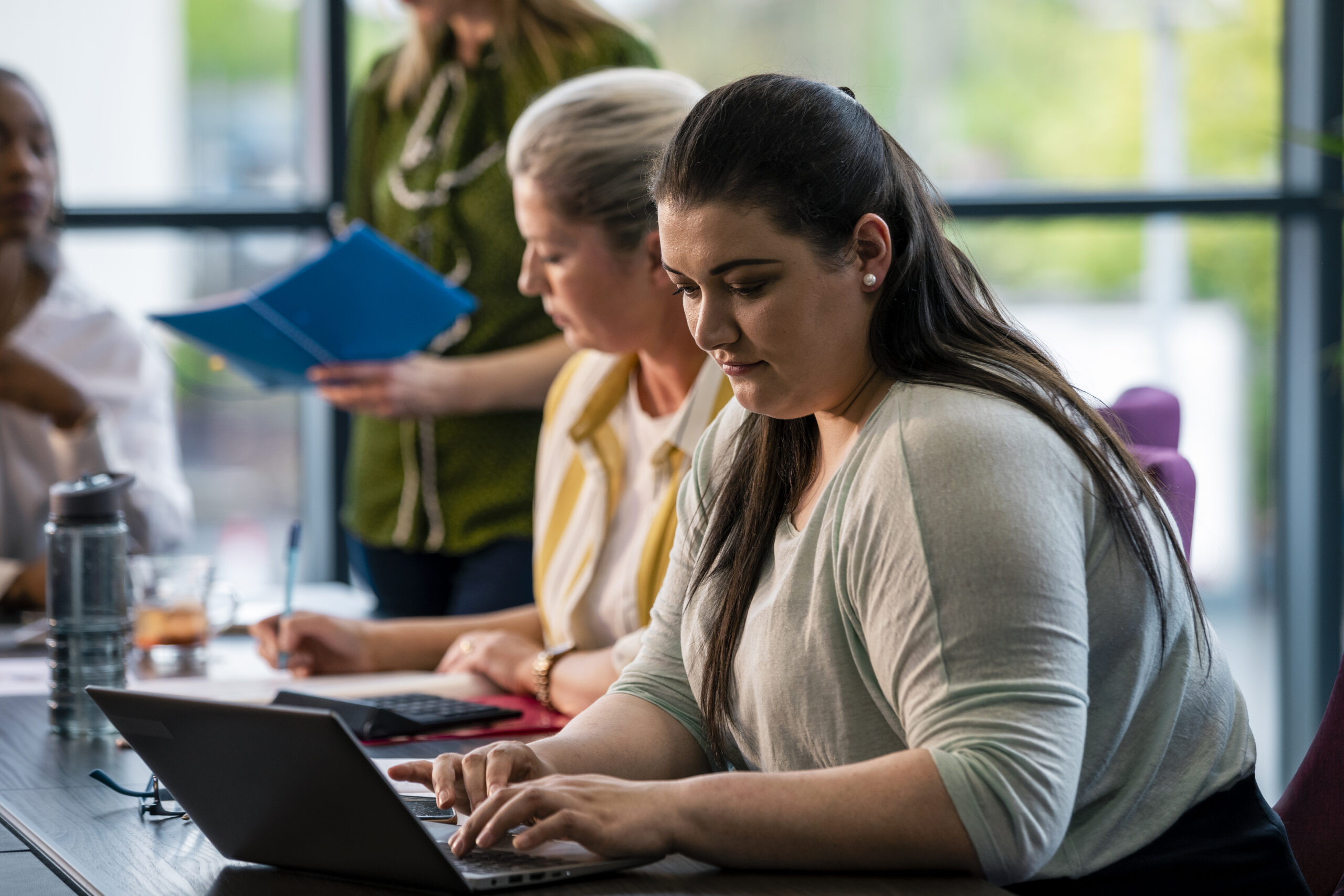 A selective focus of a woman sitting at the board room table and making notes on the managers meeting in their office.