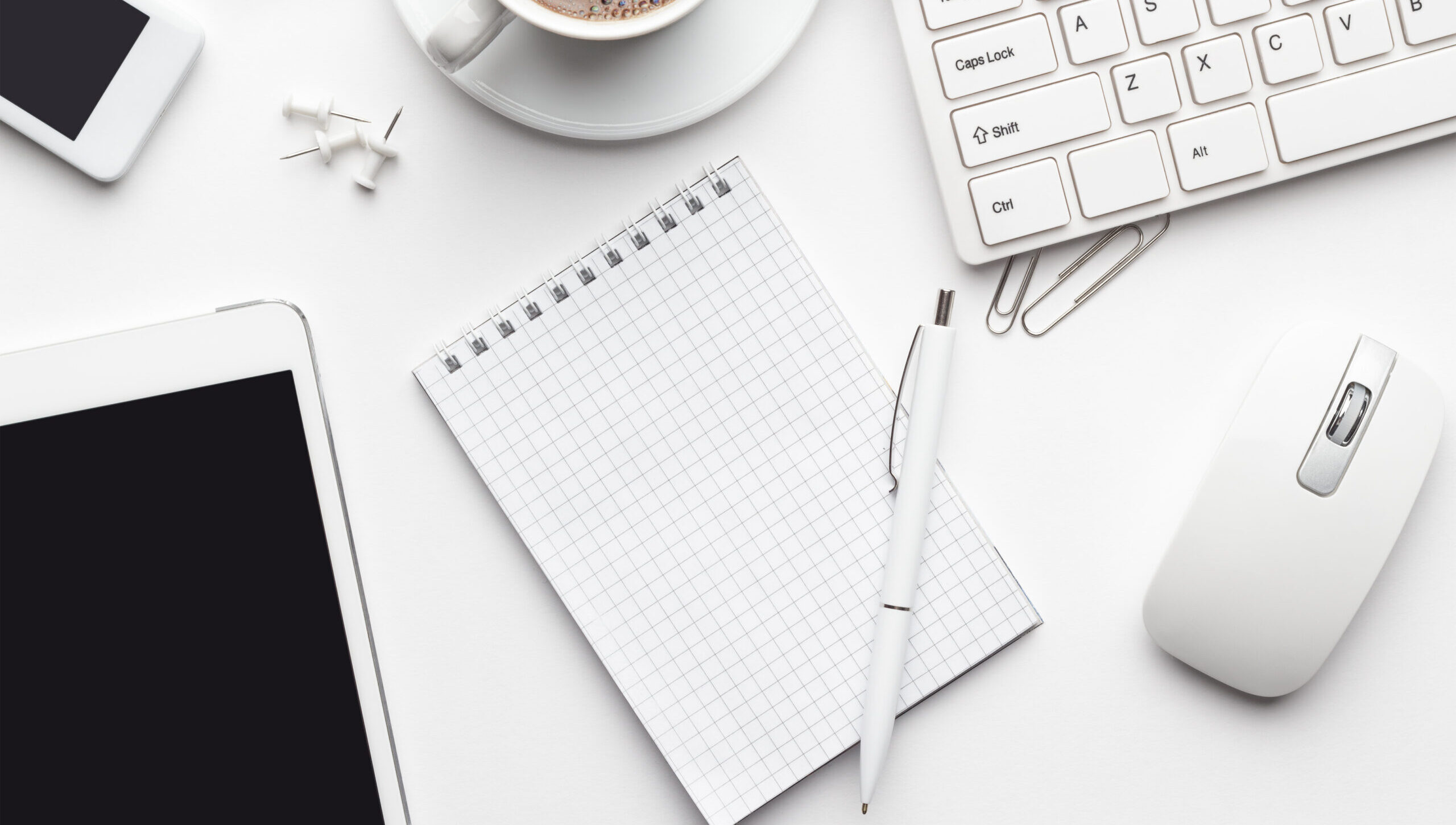 overhead of white office table with notebook, computer keyboard and mouse, tablet pc and smartphone